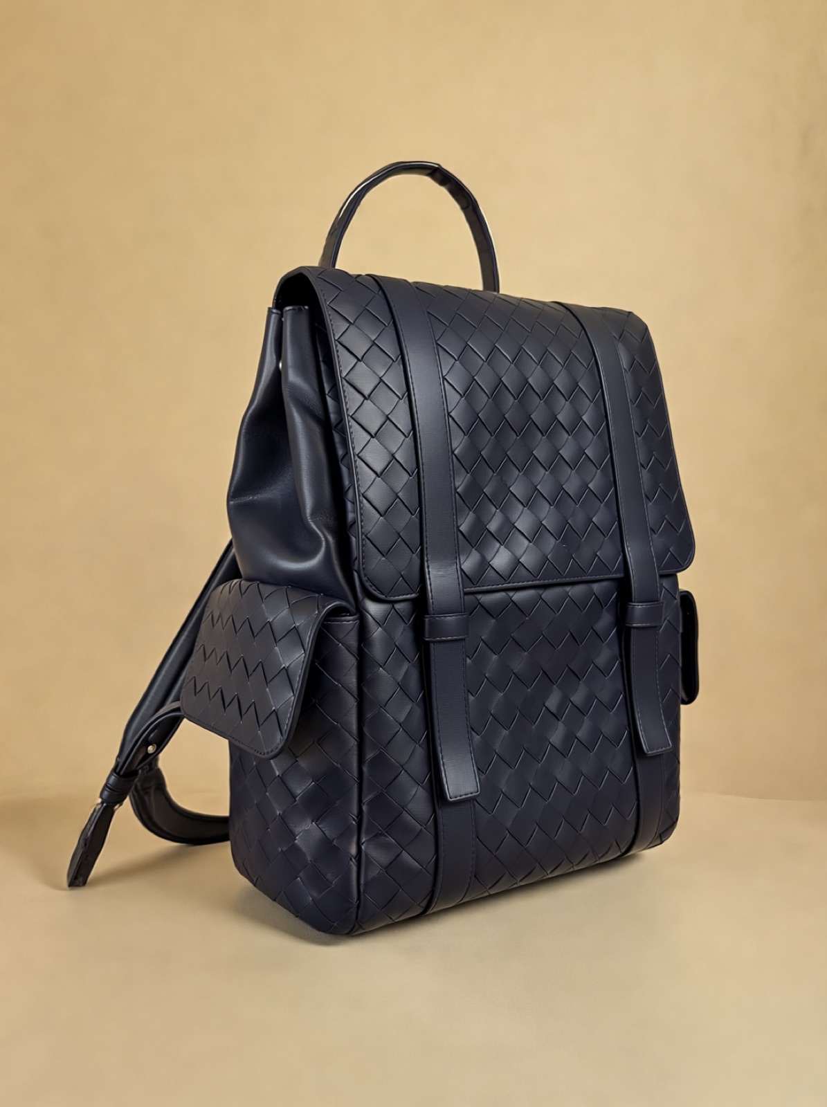 The backpack at an angle on a sand-coloured background, handle up