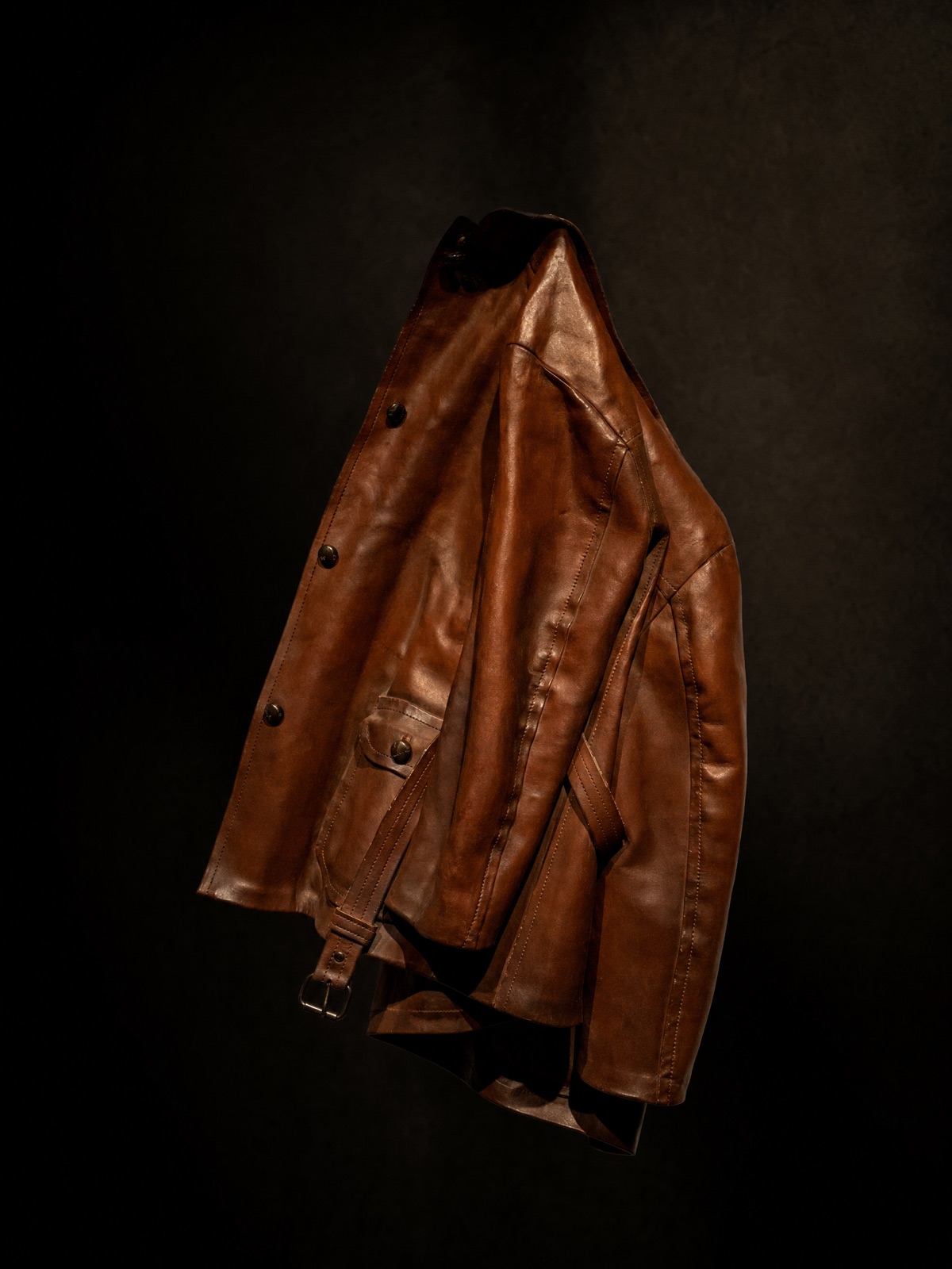 A brown leather jacket hanging against a dark backdrop with dramatic light